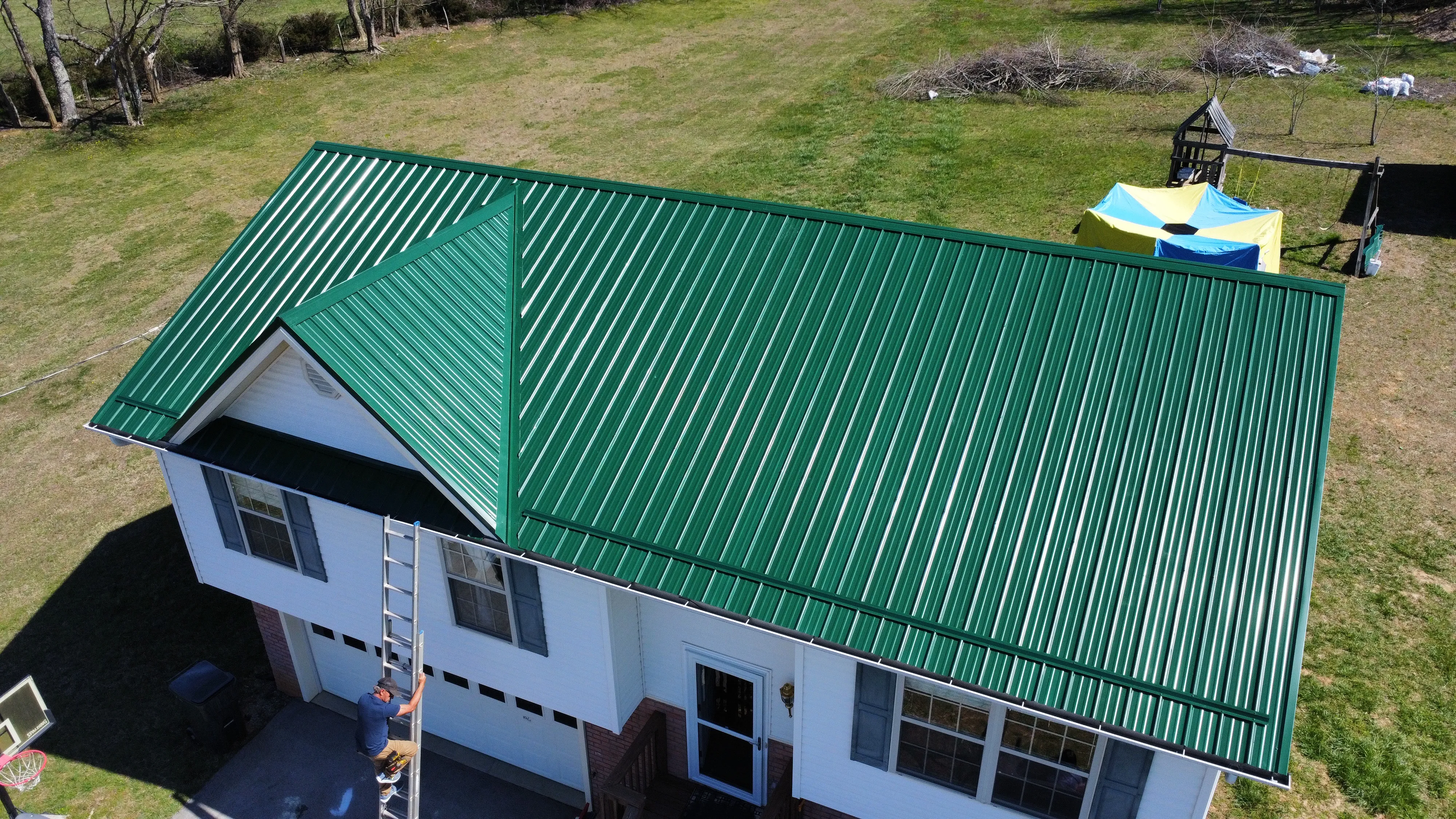 Roofer with a ladder at a home with a new green metal roof in Bristol, TN